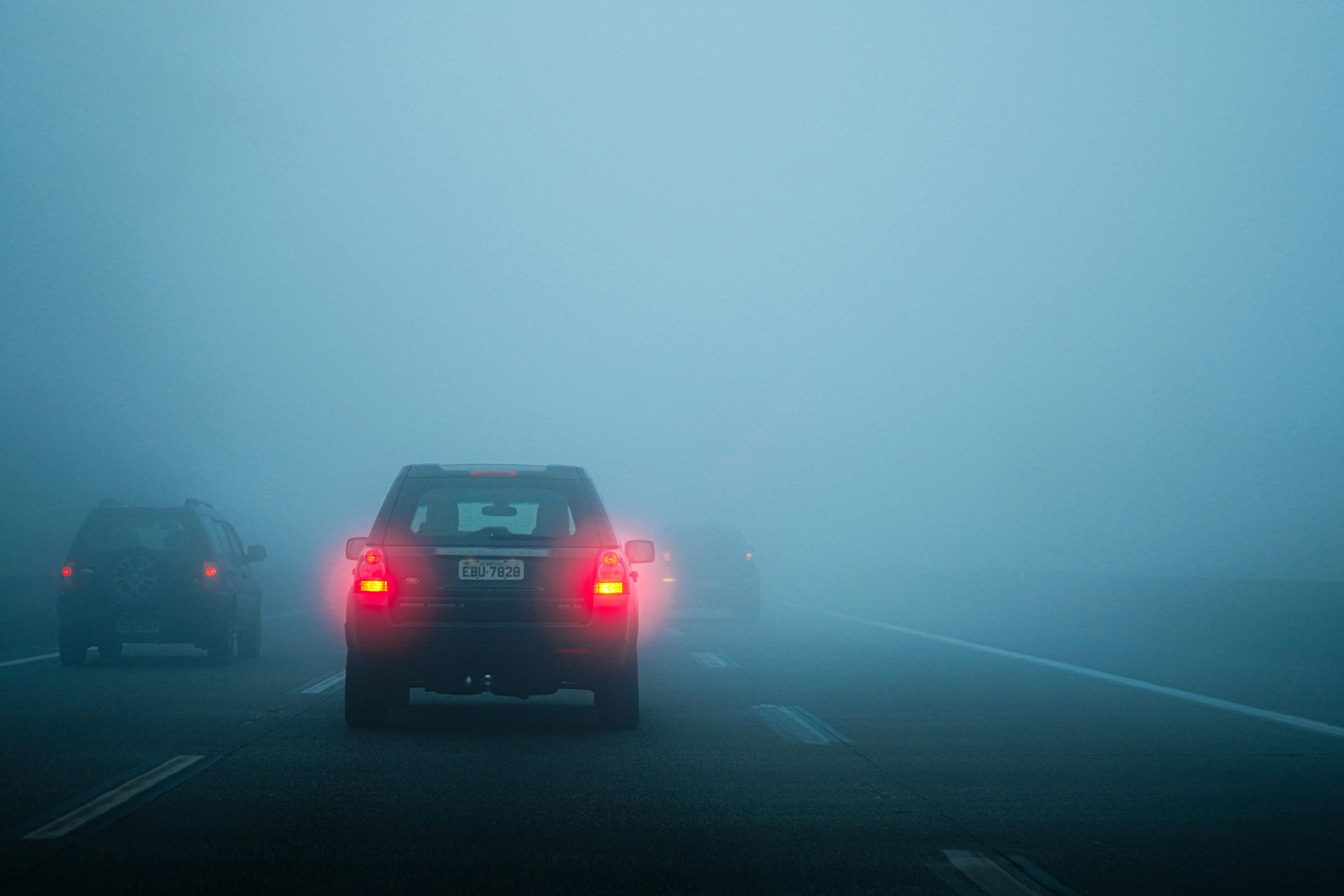 Cars with red taillights driving on a foggy highway.