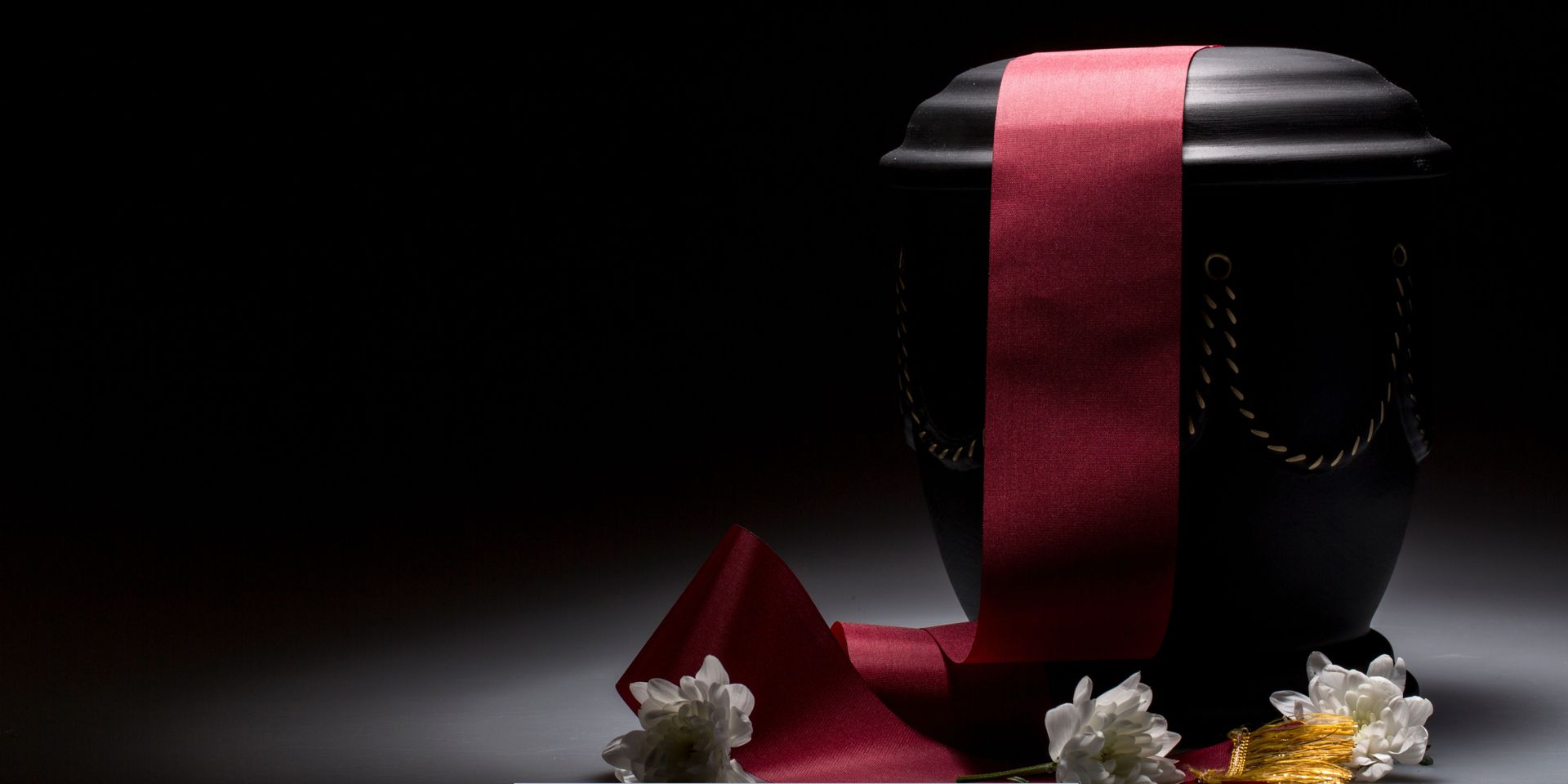 Black cremation urn with red ribbon and white flowers representing Cremation Services in Cherry Hill, NJ.