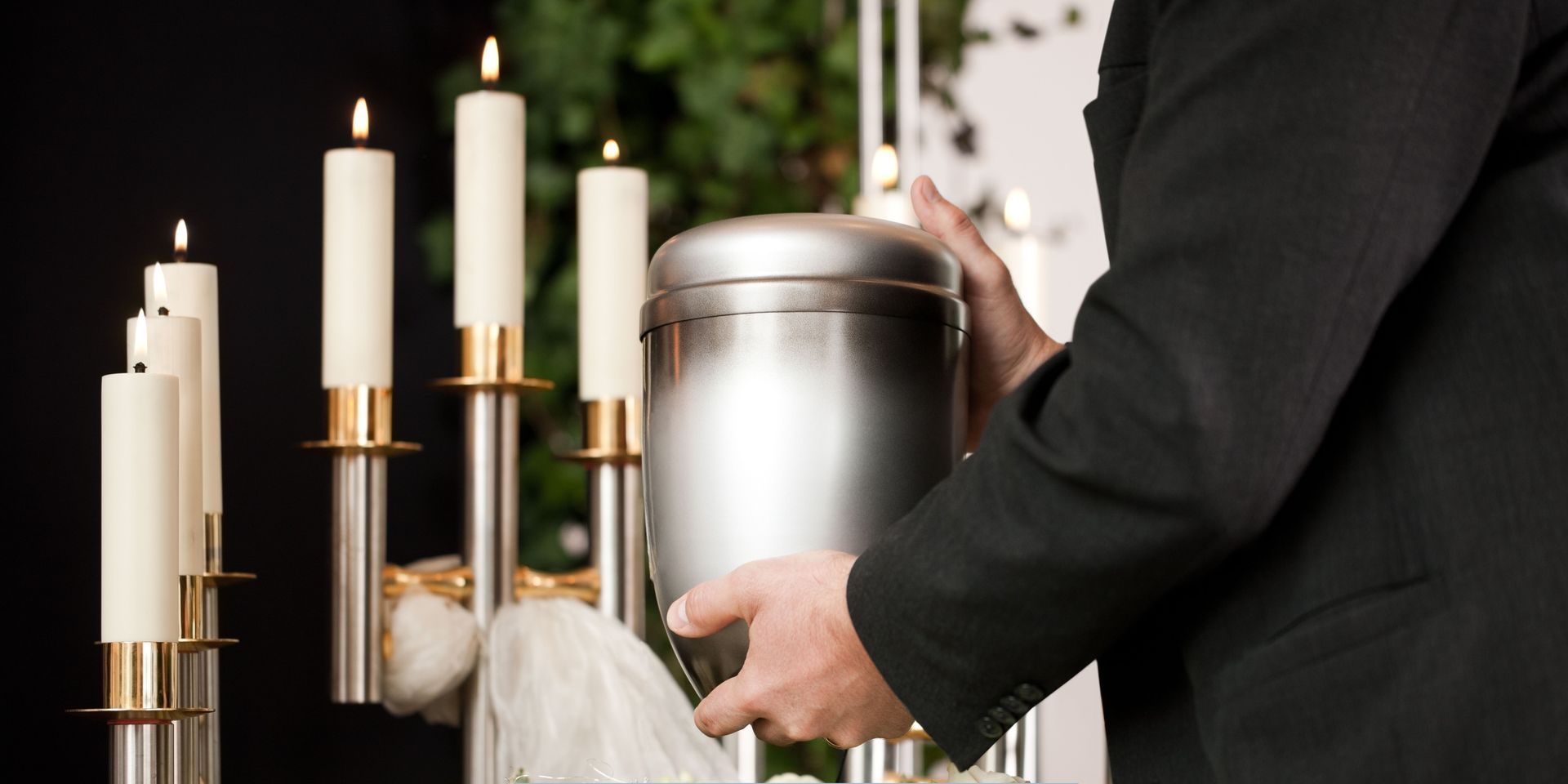 Person holding a silver cremation urn beside lit candles during a memorial for Cremation Services in Cherry Hill, NJ.