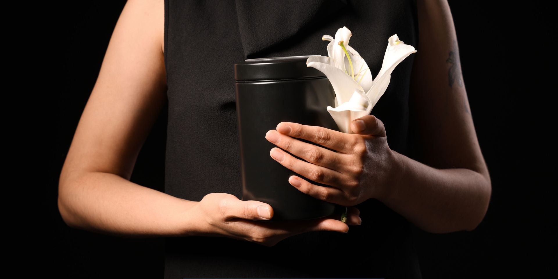 Person holding a black cremation urn with a white lily representing Cremation Services in Pennsauken Township, NJ.