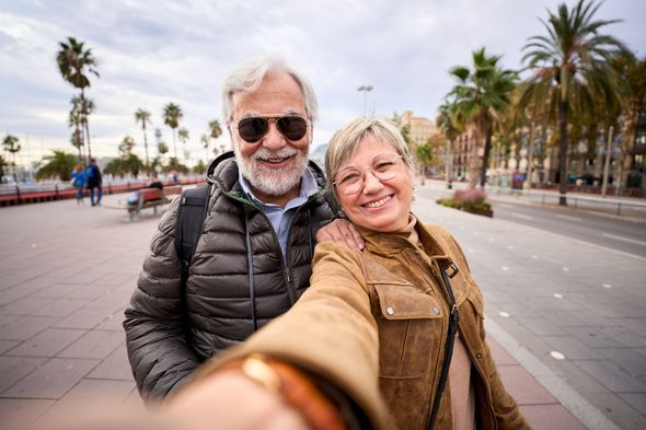 Selfie of two smiling people on a palm-lined seaside promenade