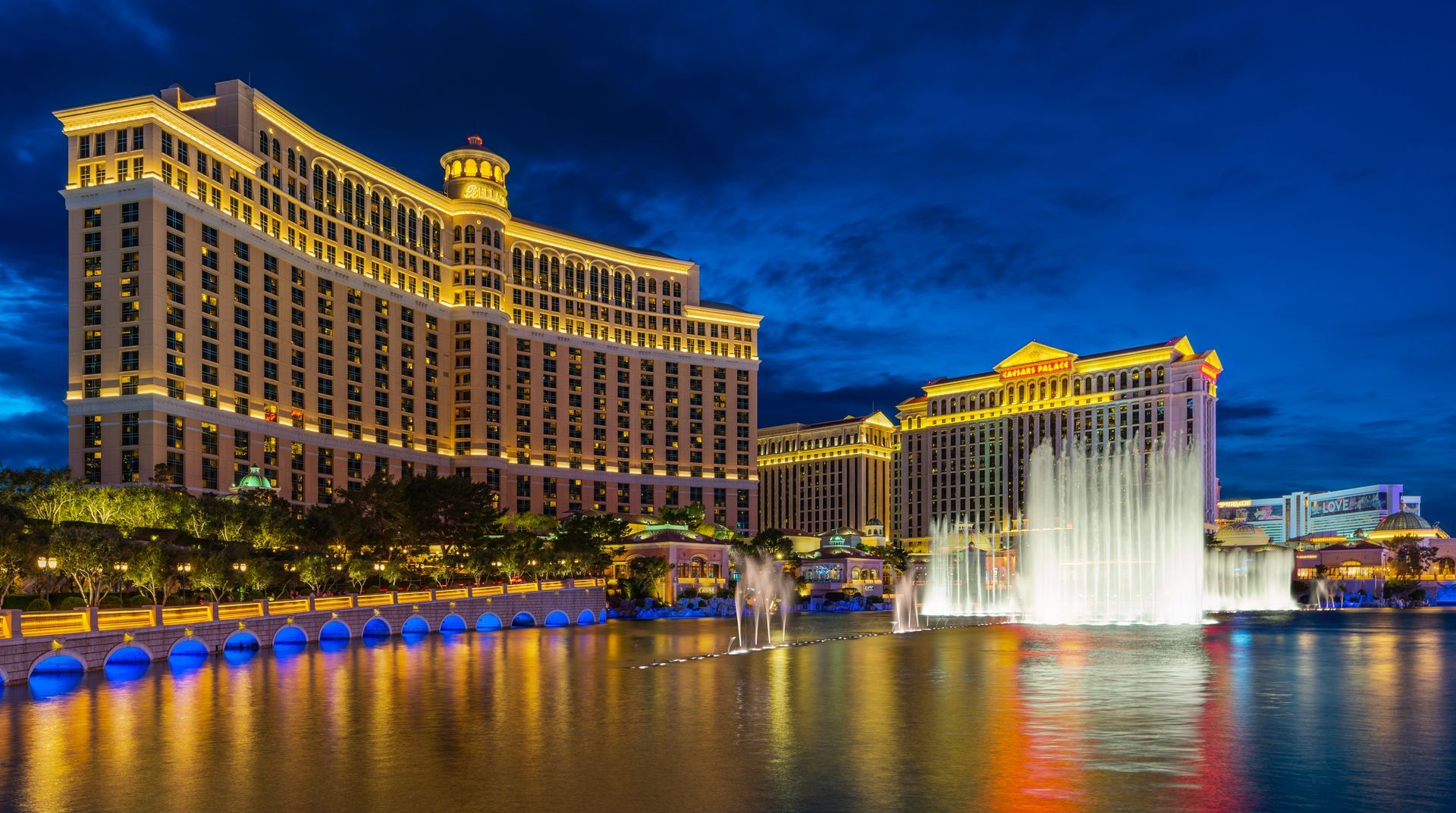 Illuminated hotel towers and a fountain reflecting on water at night, likely along the Las Vegas Strip