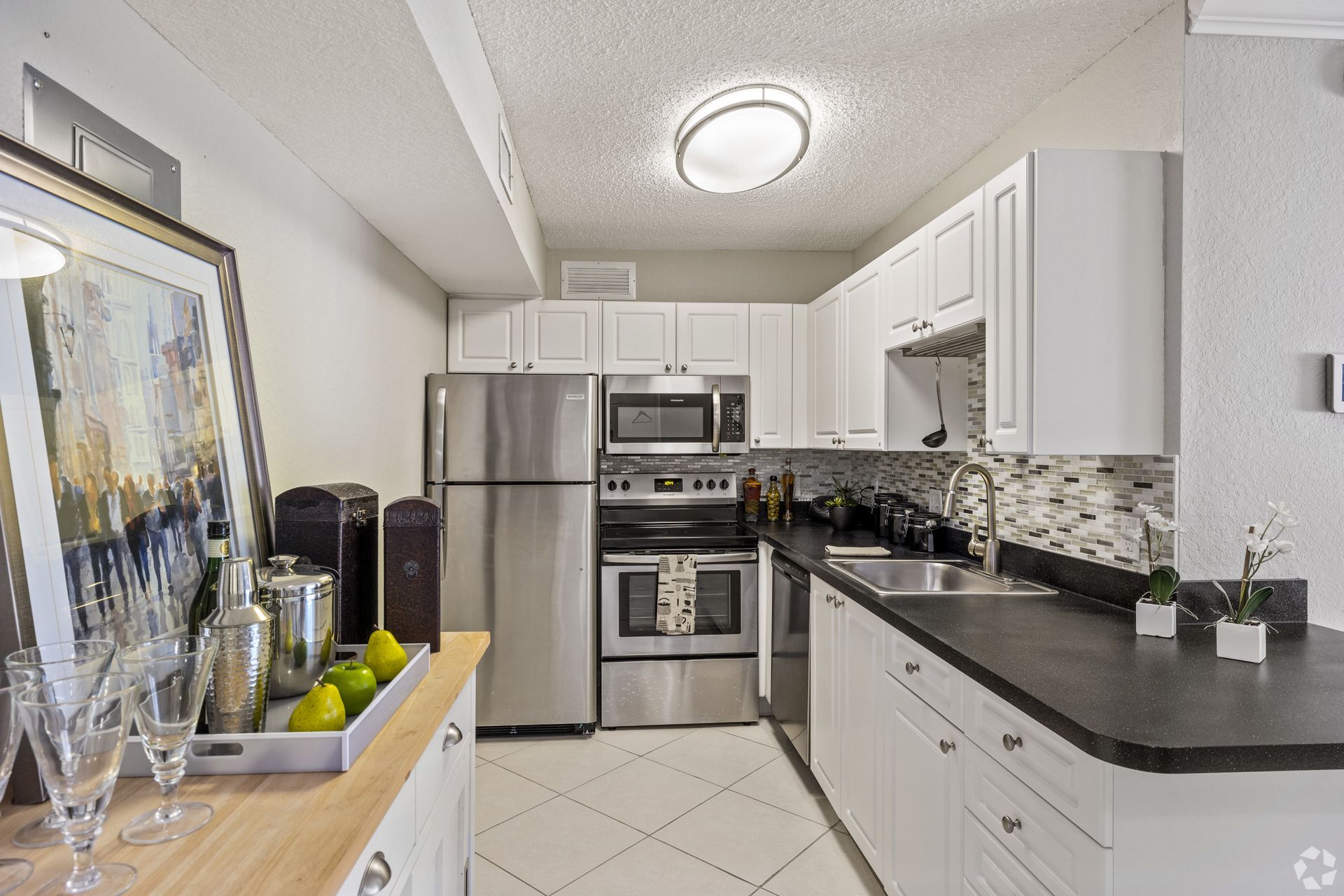 Bright modern kitchen with stainless steel appliances, white cabinets, black countertops, and tiled floor at 4120 at  Palm Beach Gardens Apartments in  FL.