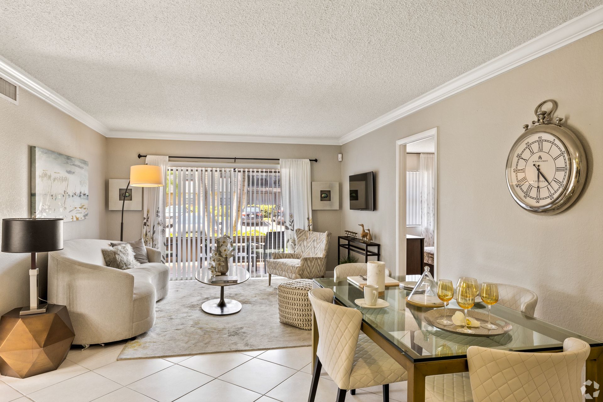 Bright living and dining room with neutral decor, glass table, armchairs, and sliding doors to a balcony at 4120 at  Palm Beach Gardens Apartments in  FL
