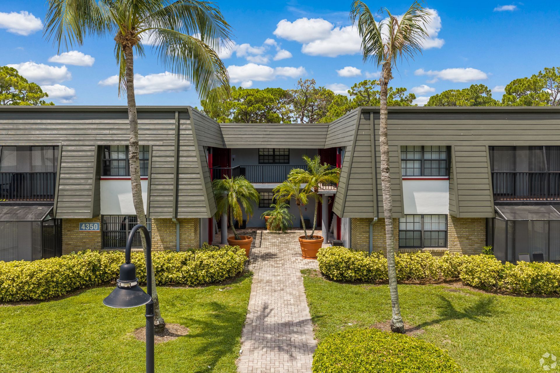 Apartment building with palm trees, trimmed hedges, and a central walkway under a clear blue sky at 4120 at Palm Beach Gardens Apartments in FL.