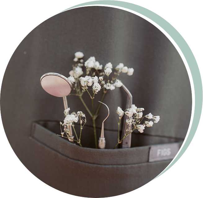 Dental tools and white flowers in a pocket of dark gray scrubs; the word 