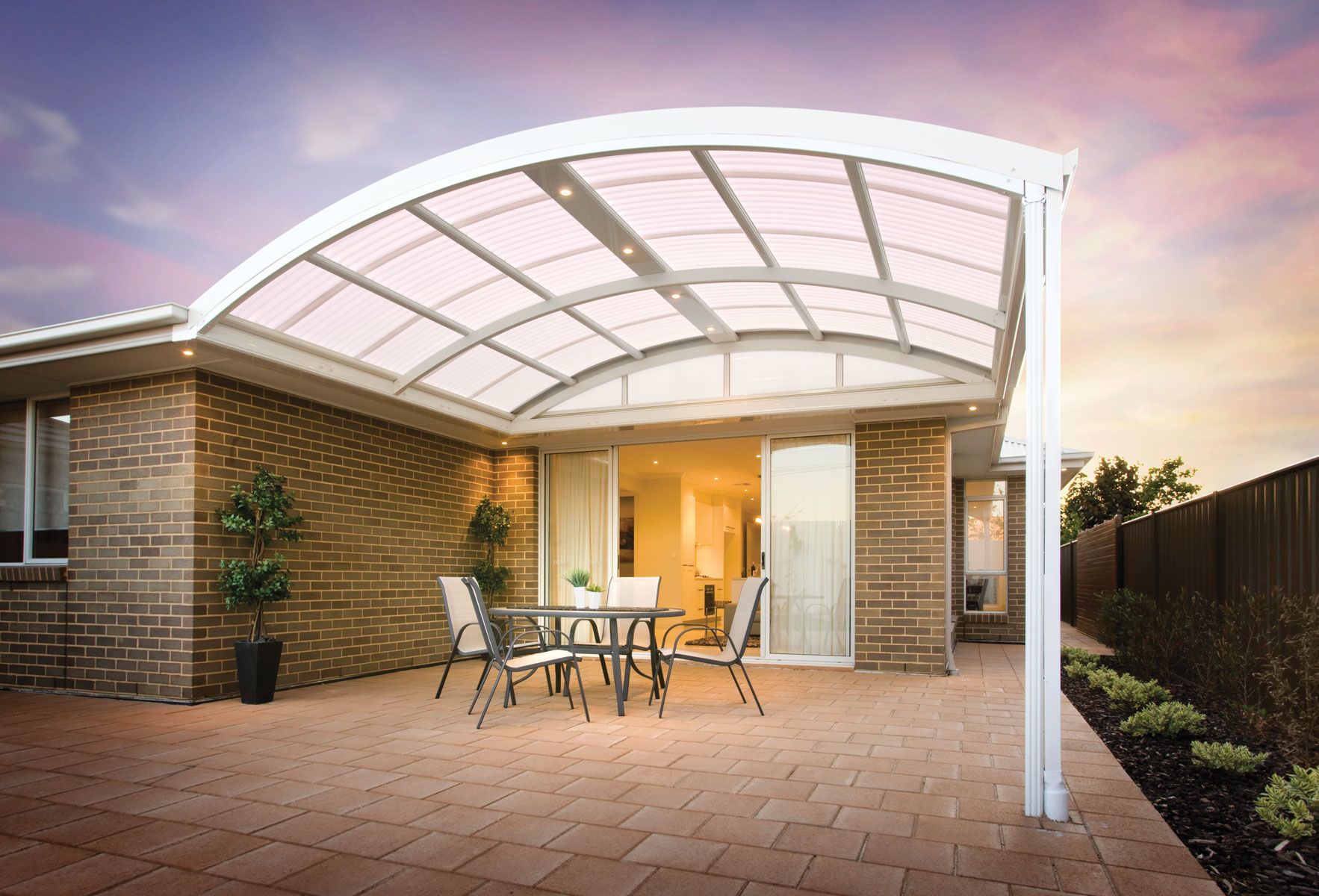 Patio with curved white roof over table and chairs, brick wall, and fence — Precision Patios Toowoomba In Toowoomba, QLD