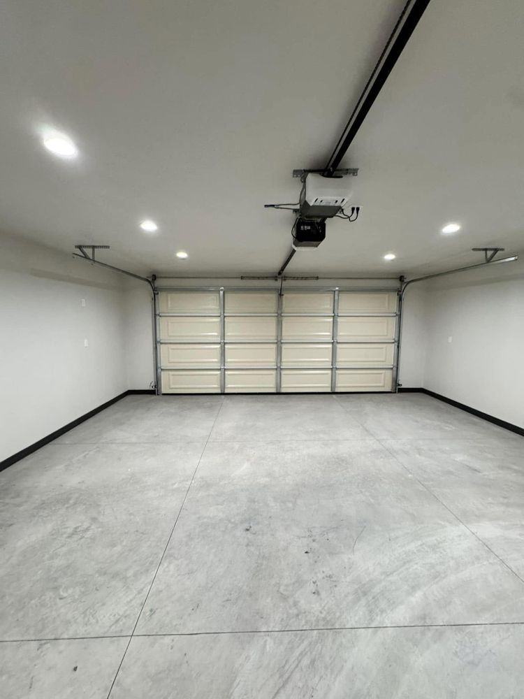 An empty garage with a garage door open and a ceiling fan.