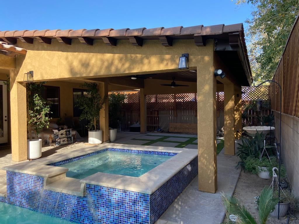 A large swimming pool with a hot tub under a pergola.