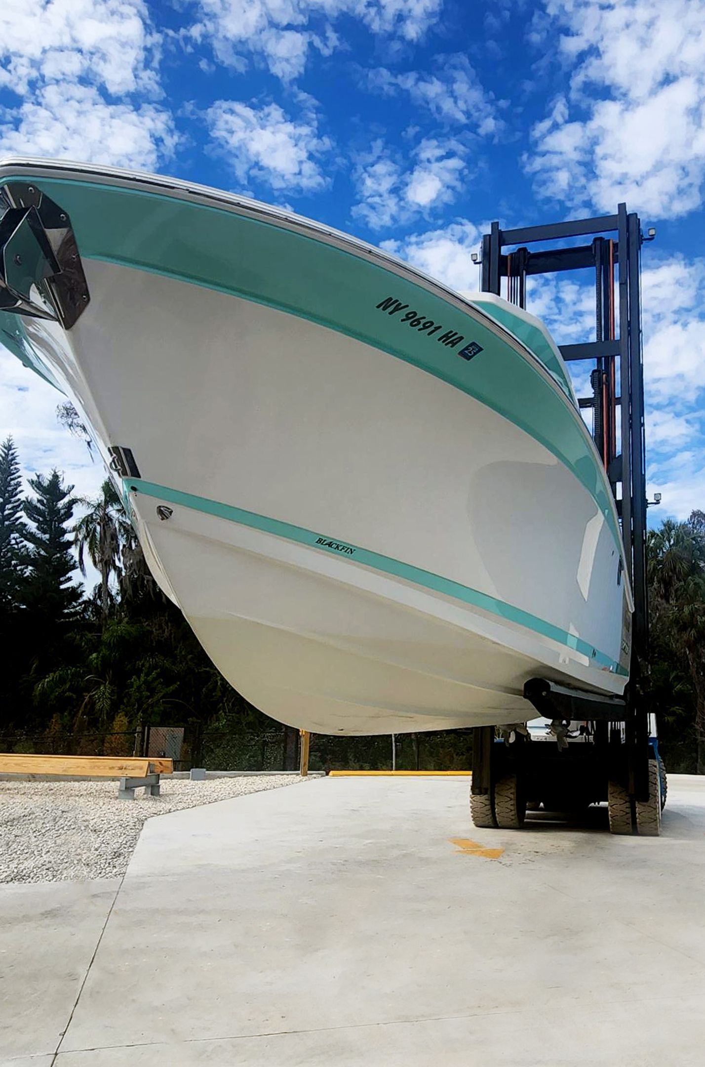 A boat is being lifted by a forklift in a parking lot at Riverview Marina
