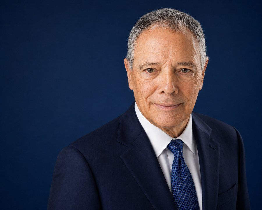 Portrait of a man in a navy suit and blue tie against a dark blue background
