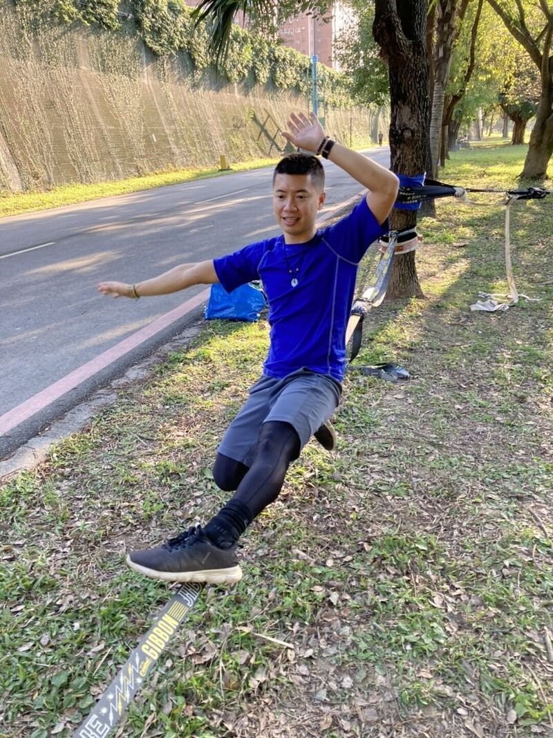 A man is doing exercises on a rope in a park.