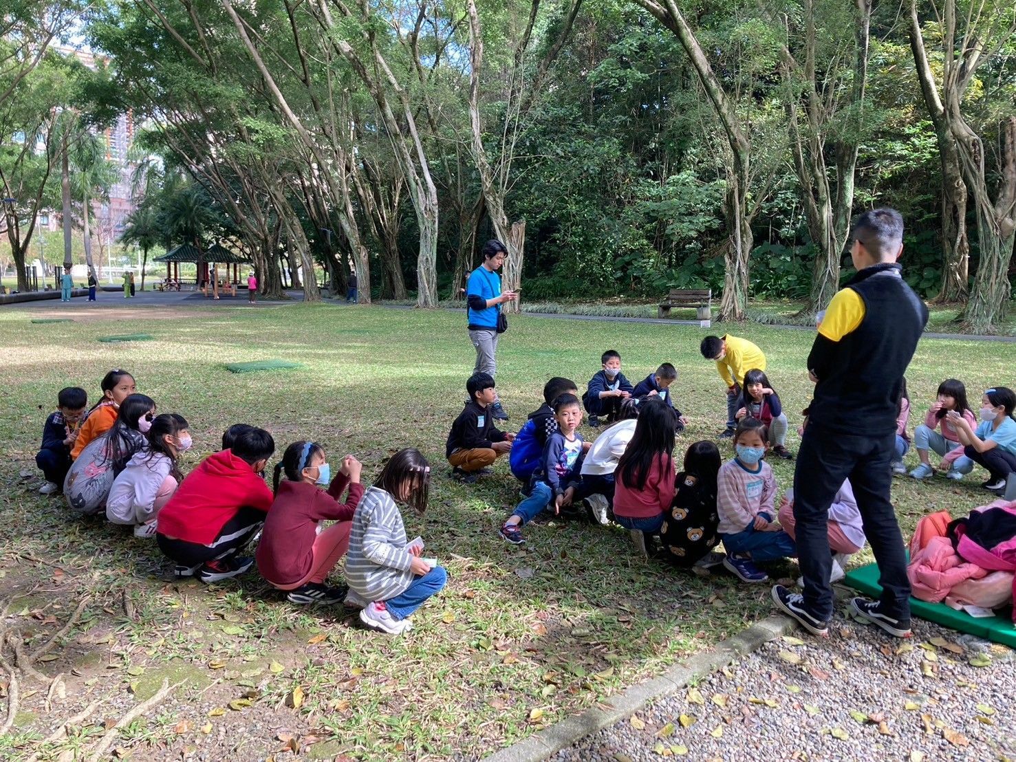 A group of children are sitting on the grass in a park.