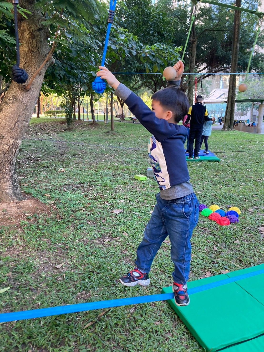 A young boy is standing on a tightrope in a park.