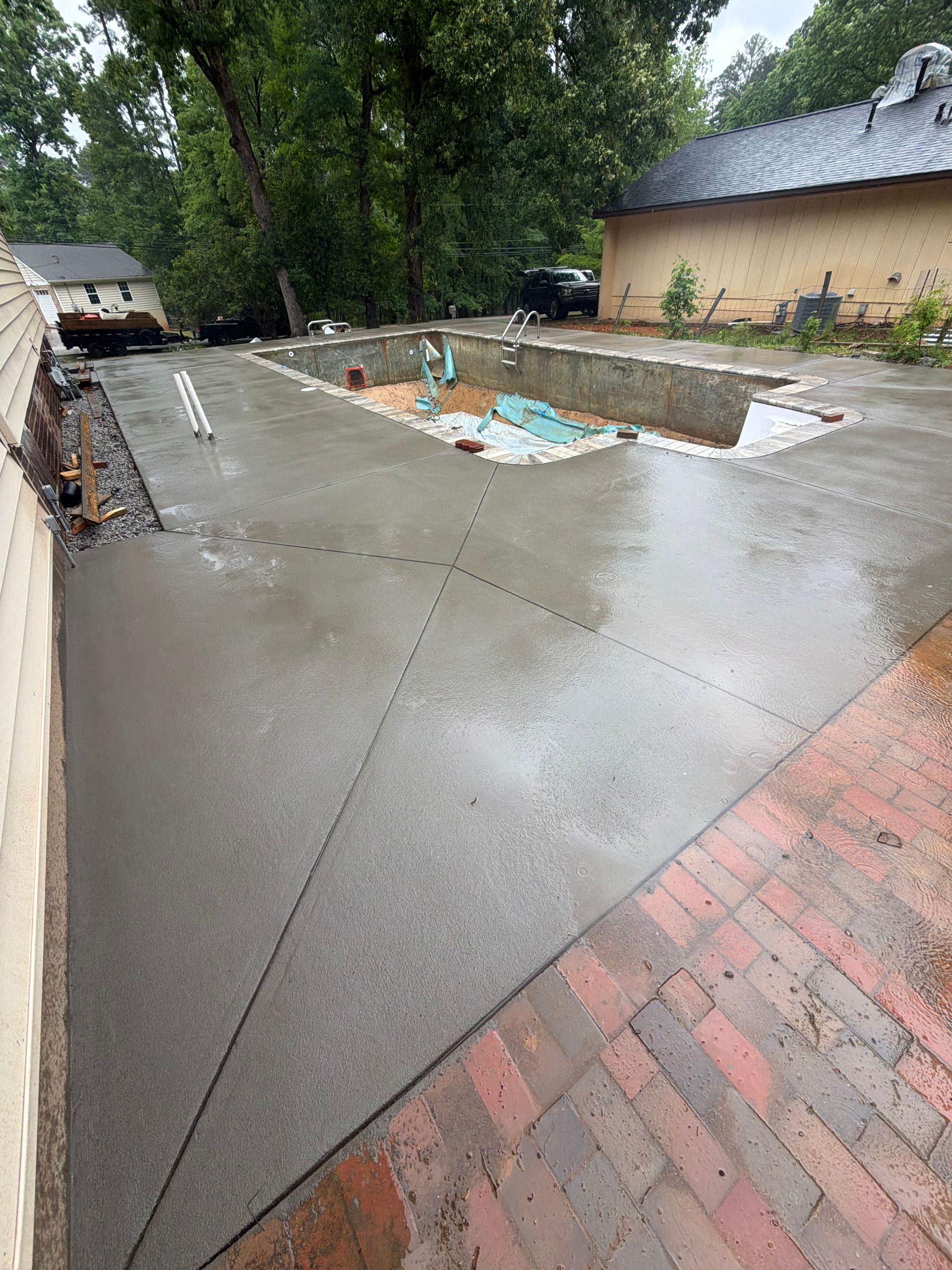 Concrete patio with textured stone pattern next to a swimming pool filled with water.