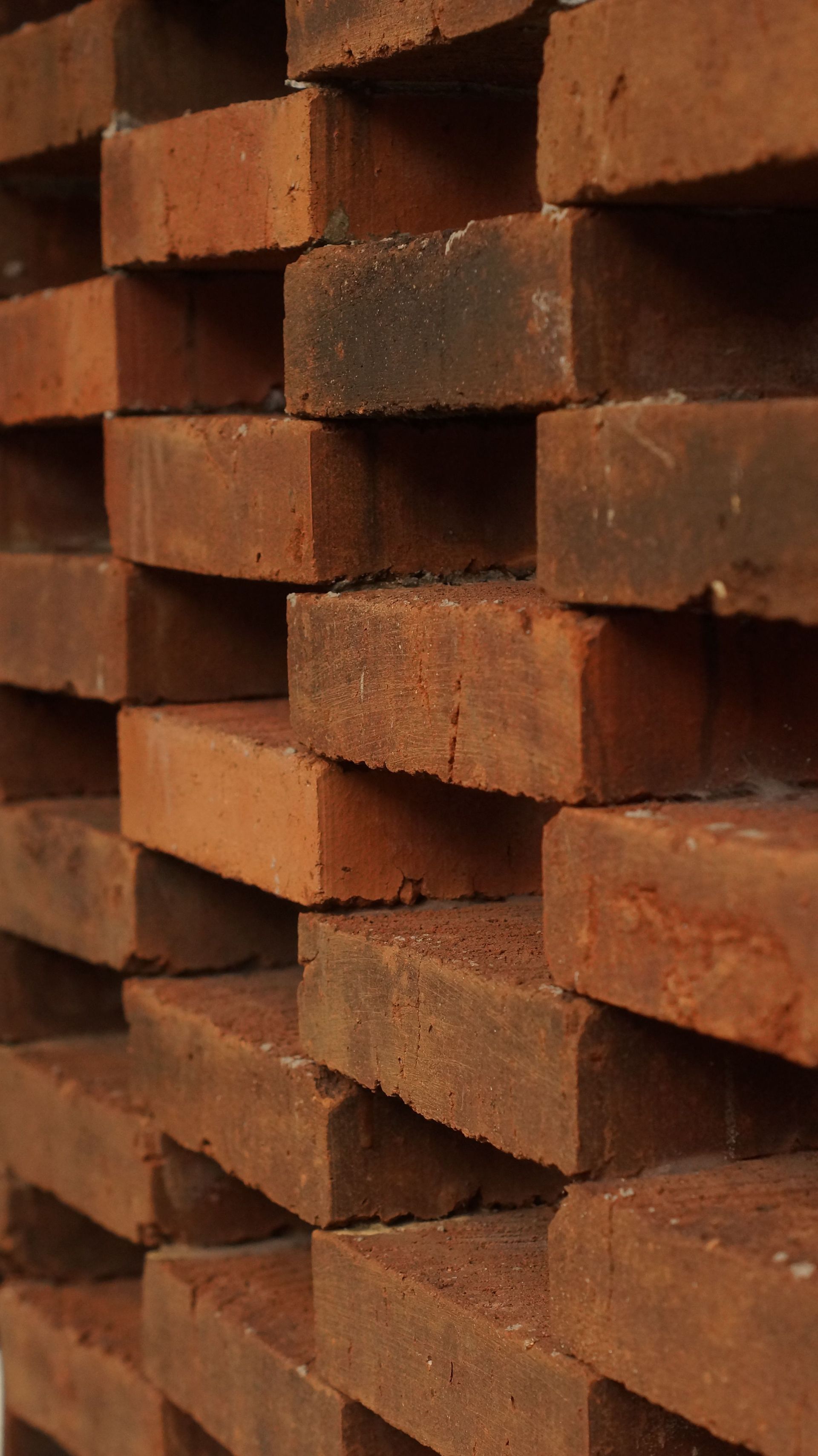 Stacked red clay bricks in a close-up view, showing rough texture and staggered layers.