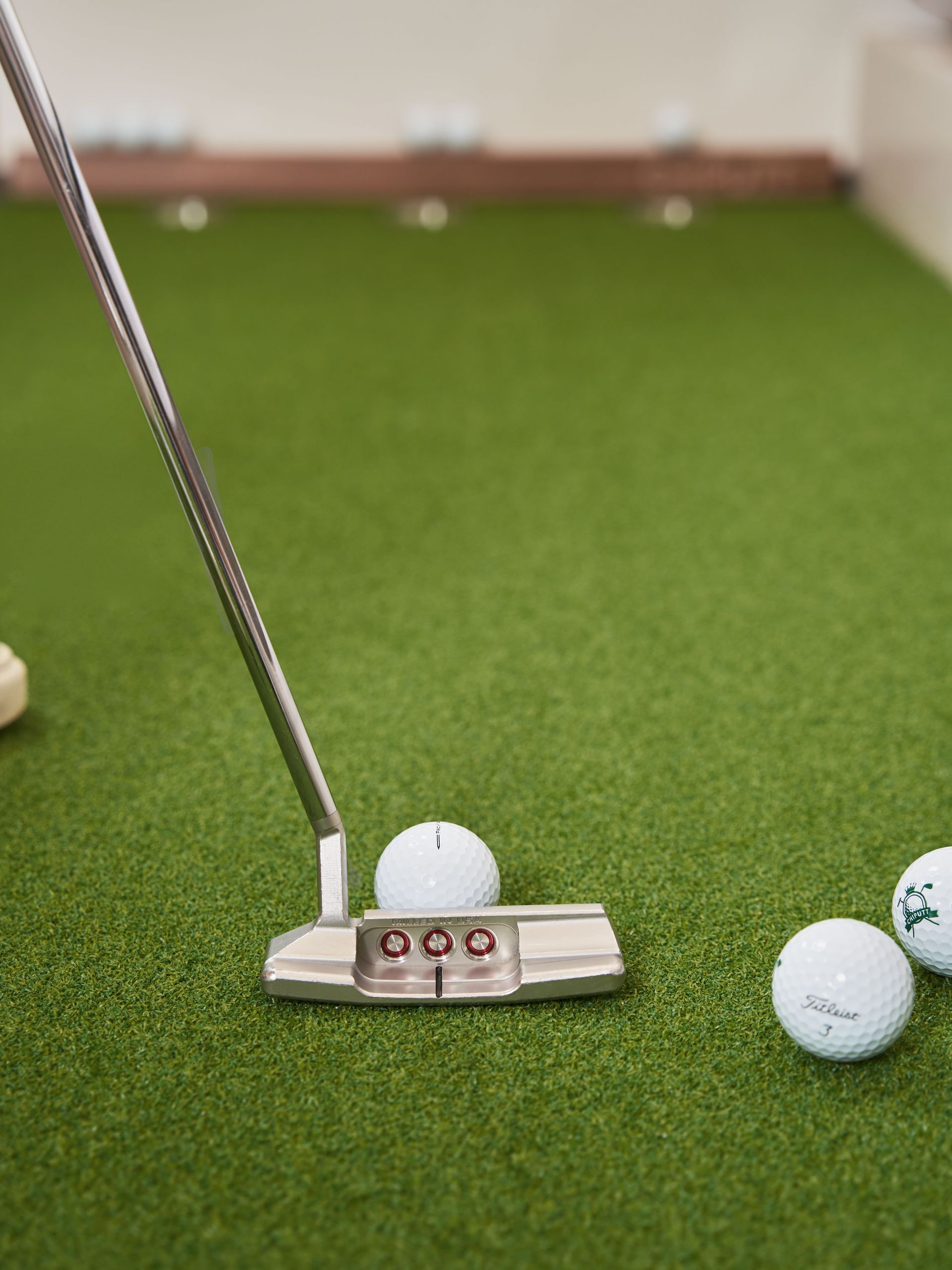 Golf putter on green turf aiming at a ball, with two balls nearby.