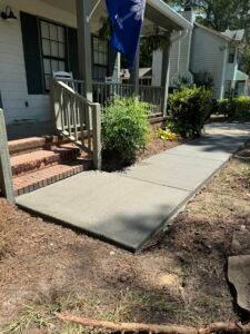 Newly poured concrete walkway leading to a house with a porch and steps.