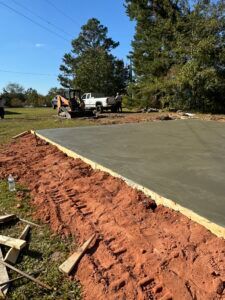 Freshly poured concrete slab, bordered by wood and red dirt, construction site with truck.