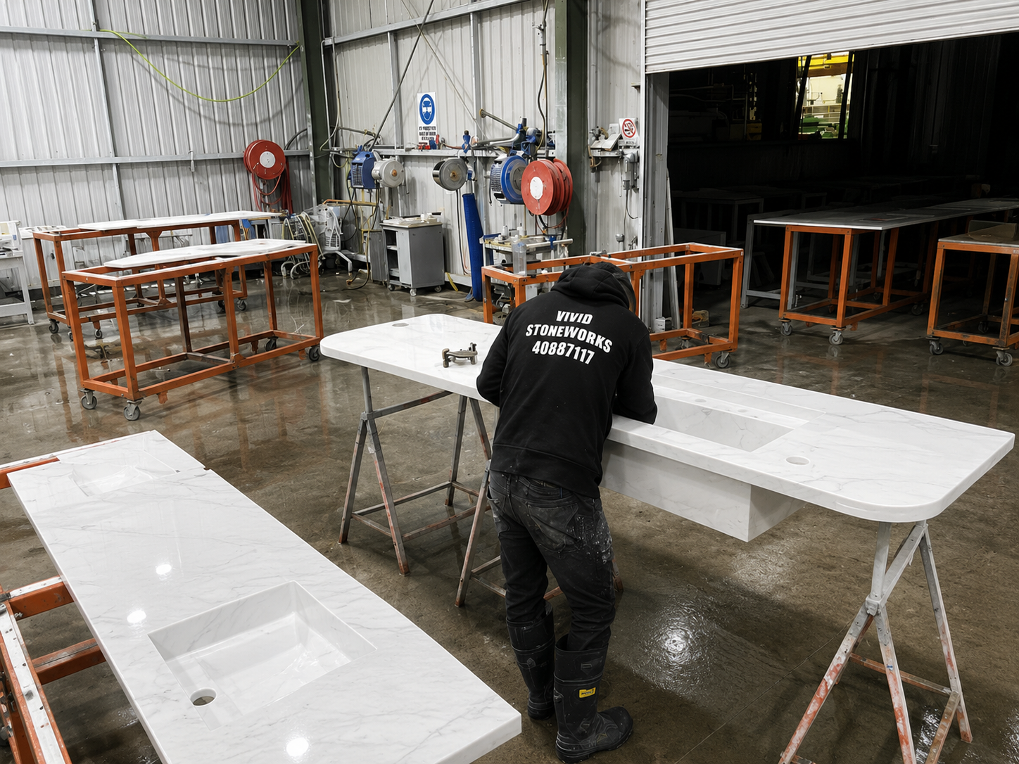 Worker sanding a white table in a workshop with other tables and tools nearby