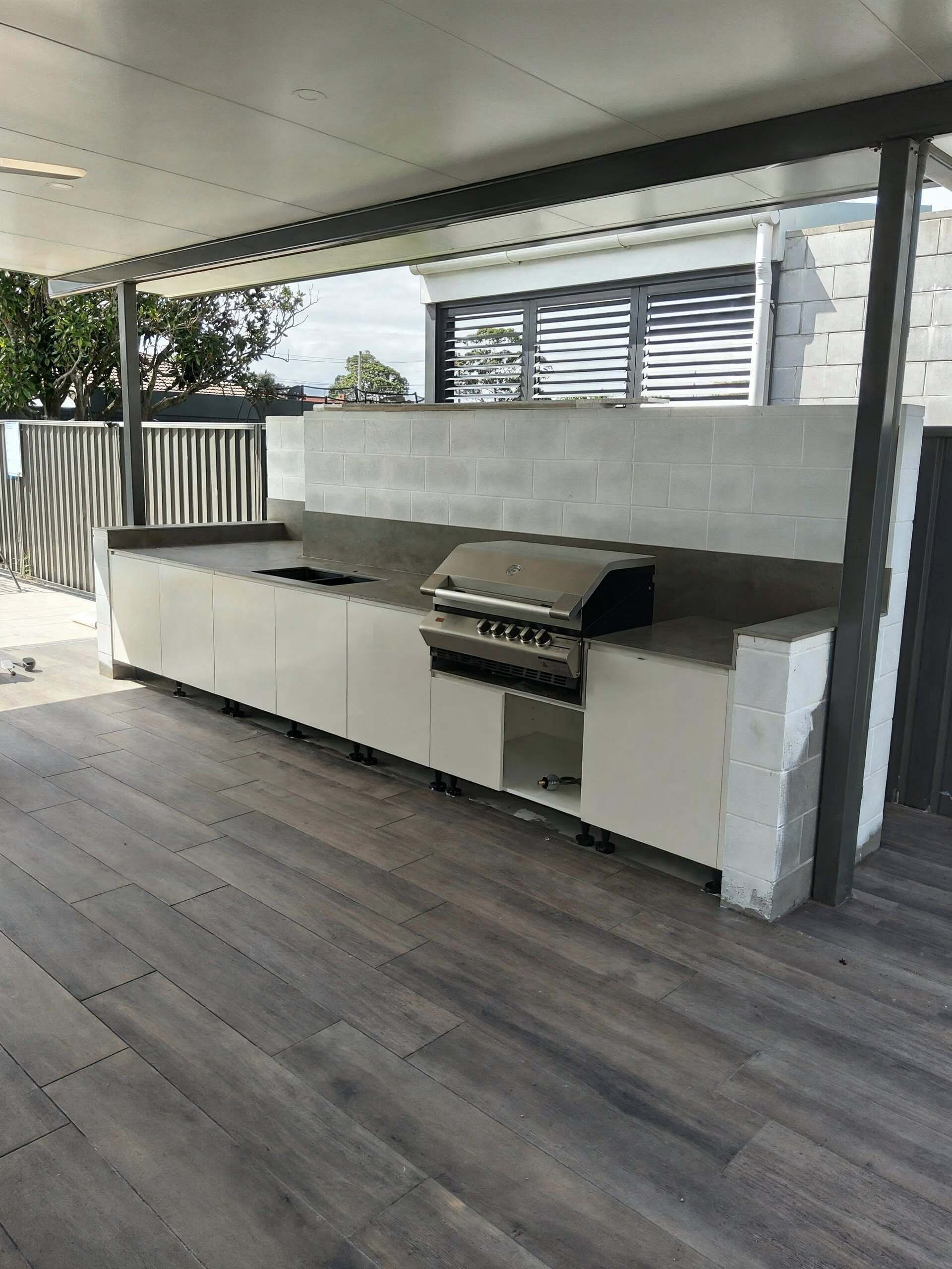 Covered outdoor kitchen with white cabinets, grill, countertop, and wood-look deck flooring