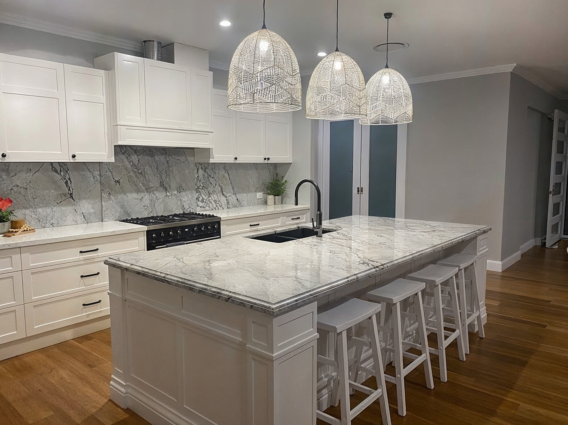 Bright white kitchen with marble island, pendant lights, bar stools, and hardwood floors