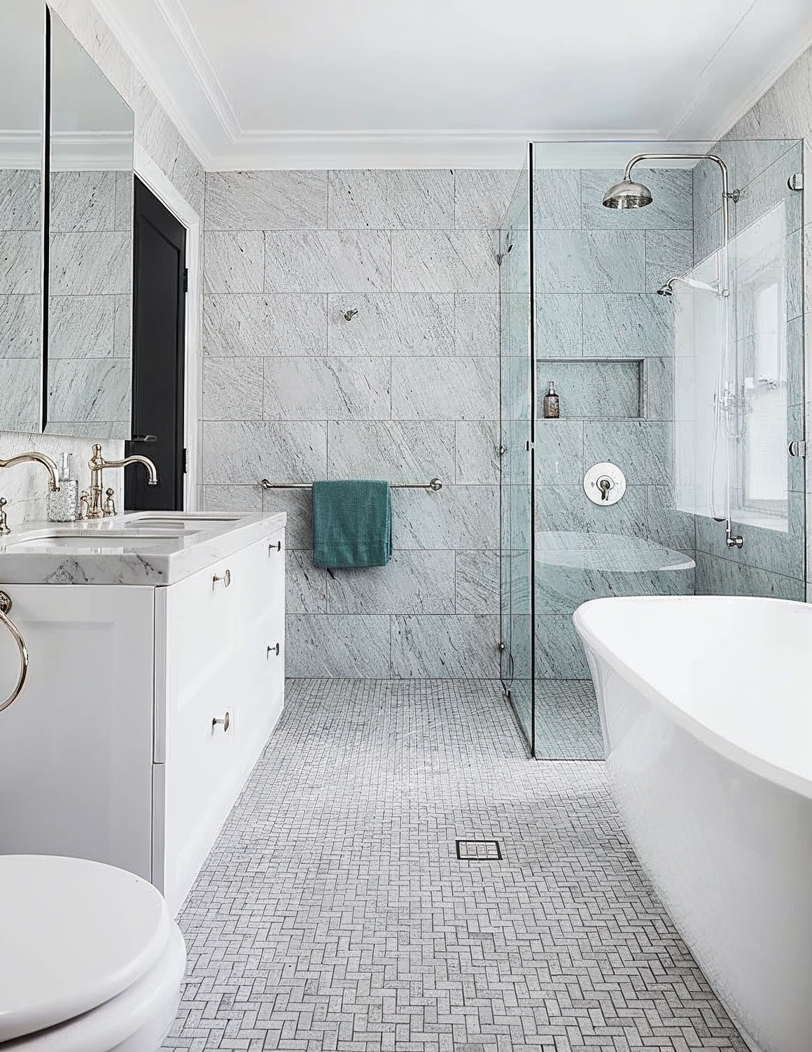 Modern gray-tiled bathroom with glass shower, vanity, toilet, and freestanding tub