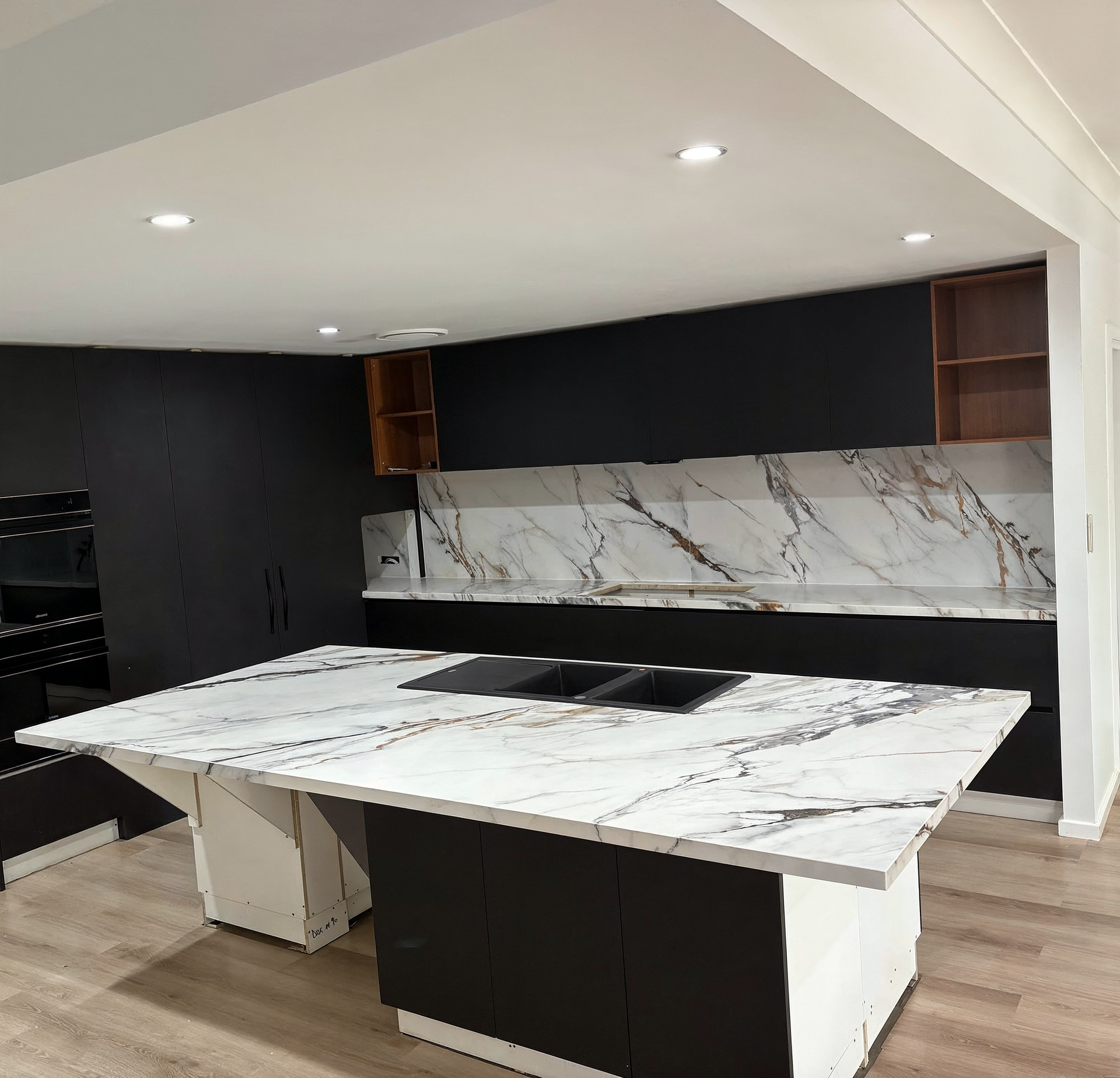 Modern kitchen with marble island, black backsplash, and recessed ceiling lights