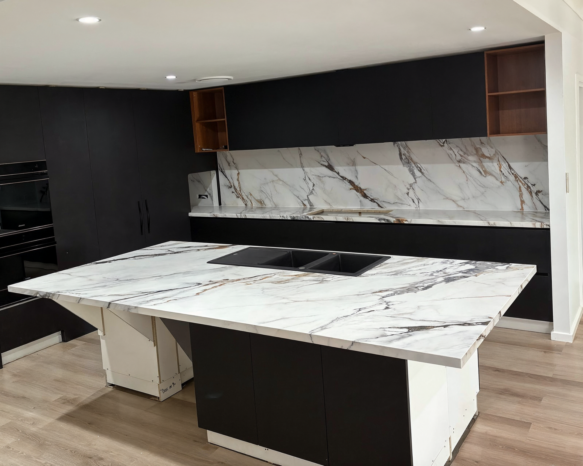 Modern kitchen with black cabinets and a white marble-look island and backsplash