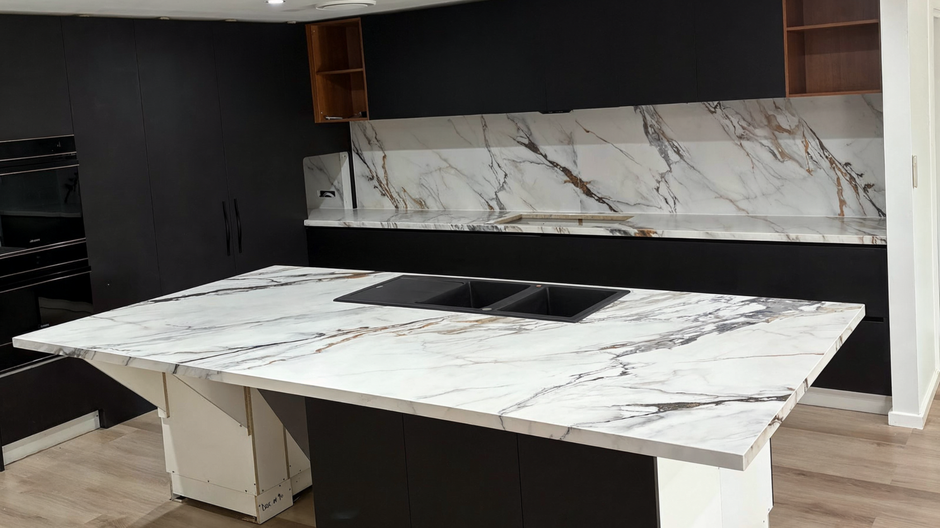 Modern kitchen with a large white marble island and matching backsplash, black cabinetry, and wood flooring