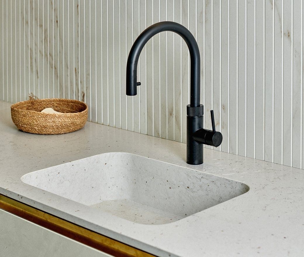 Modern kitchen sink with black faucet on a light countertop, next to a wicker basket.