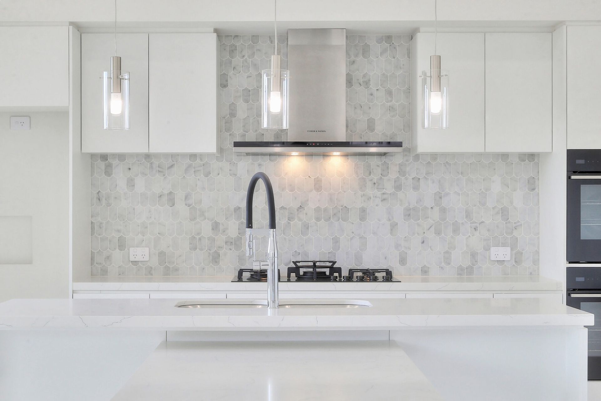 Modern white kitchen with island, pendant lights, marble backsplash, and stainless-steel range hood