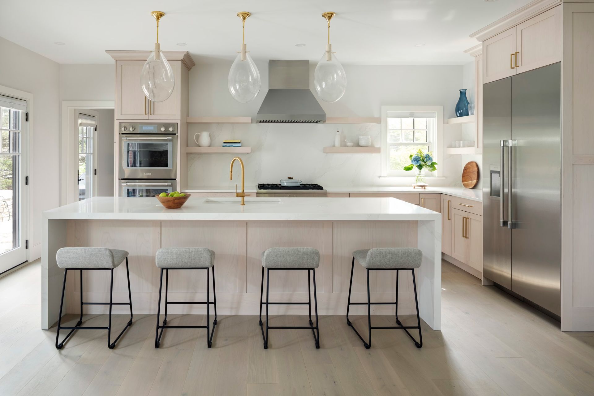 Bright modern kitchen with white cabinets, marble island, four stools, and stainless steel appliances