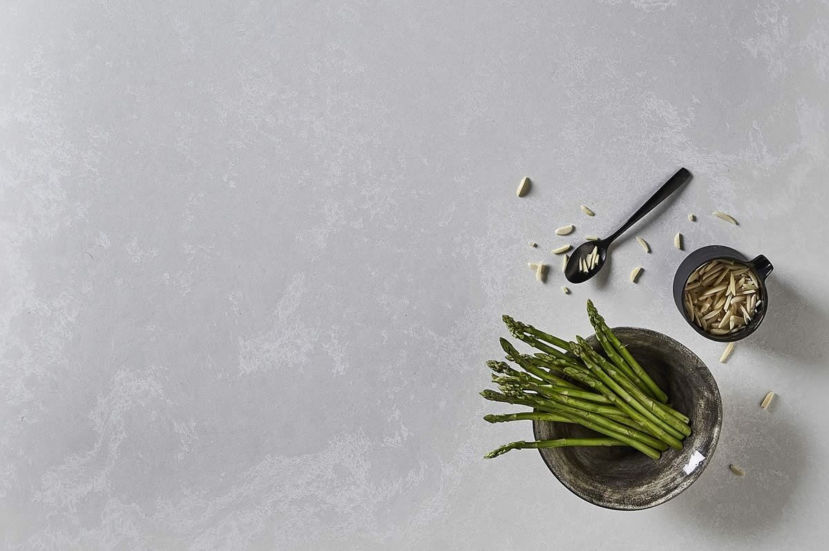 Green asparagus and small bowls of ingredients on a gray surface, viewed from above