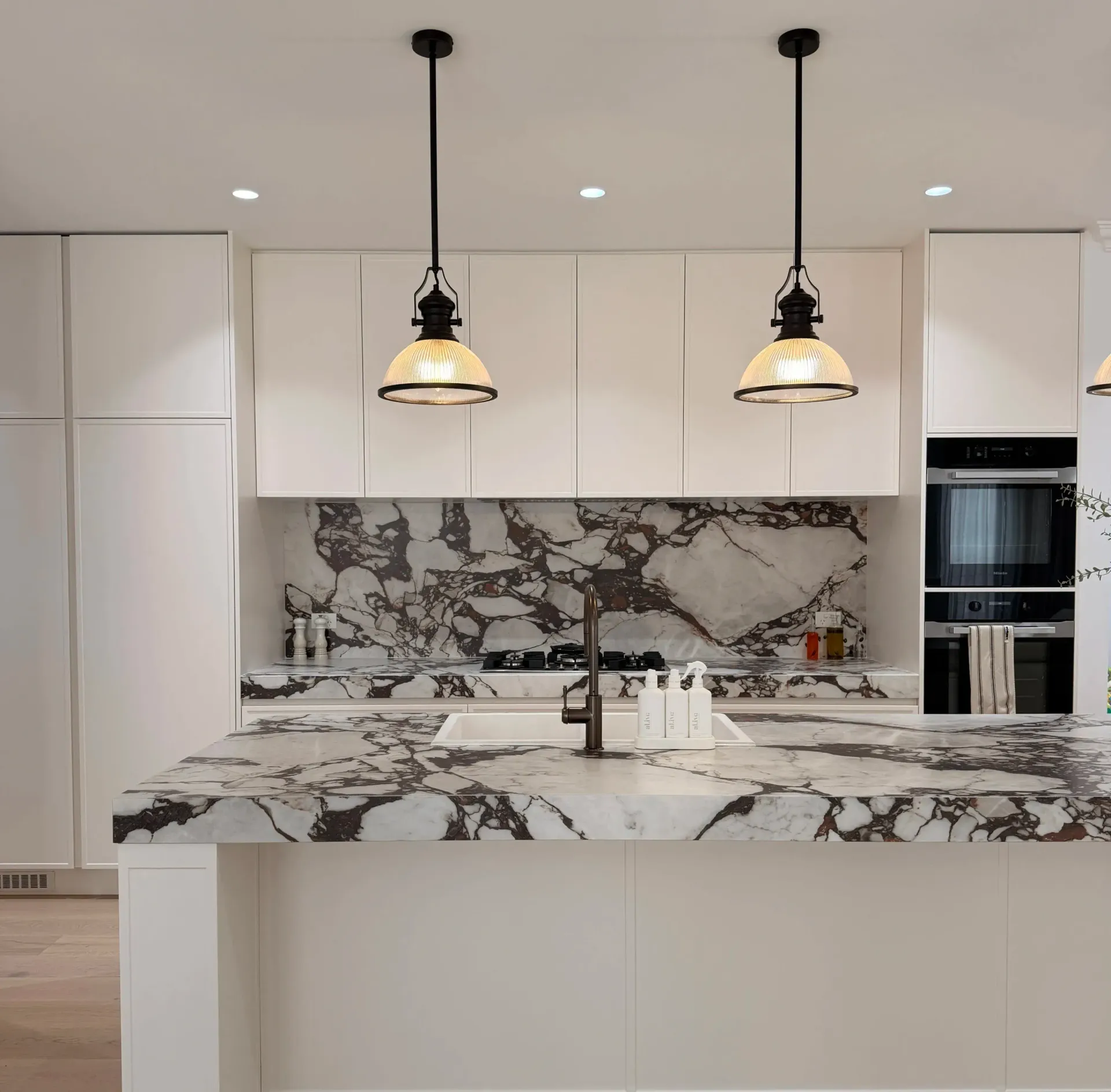 Modern white kitchen with marble island, black pendant lights, and matching marble backsplash