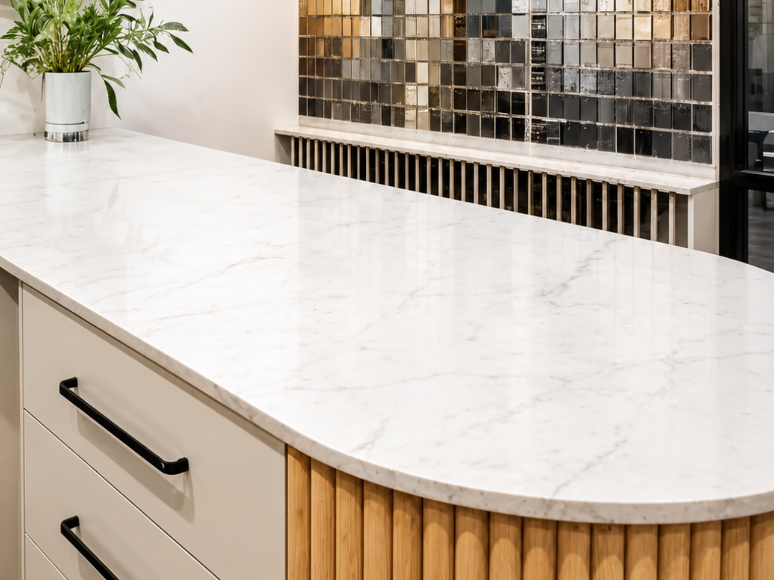 White marble kitchen island countertop with black pulls, wood slatted base, and mosaic tile backsplash