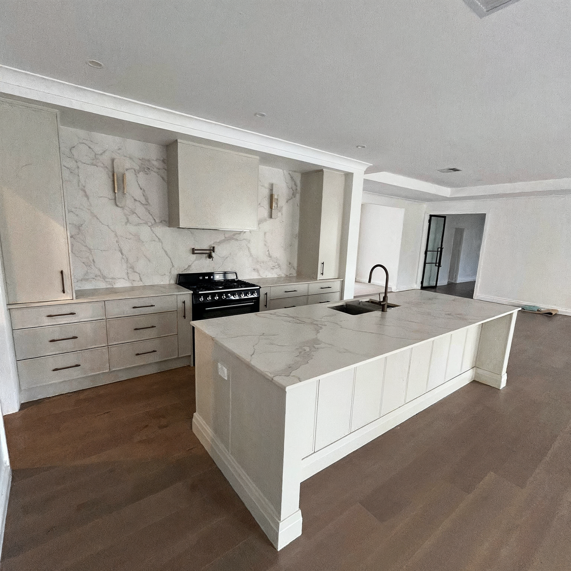 Modern kitchen with a large white island, black cabinetry, and pendant lights by a bright window.
