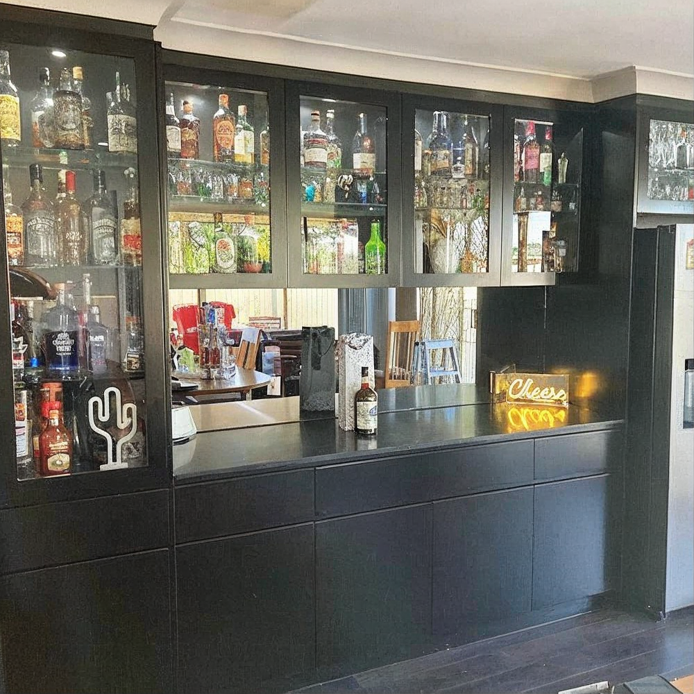 Black home bar with glass cabinets, liquor bottles, and a neon sign on the counter