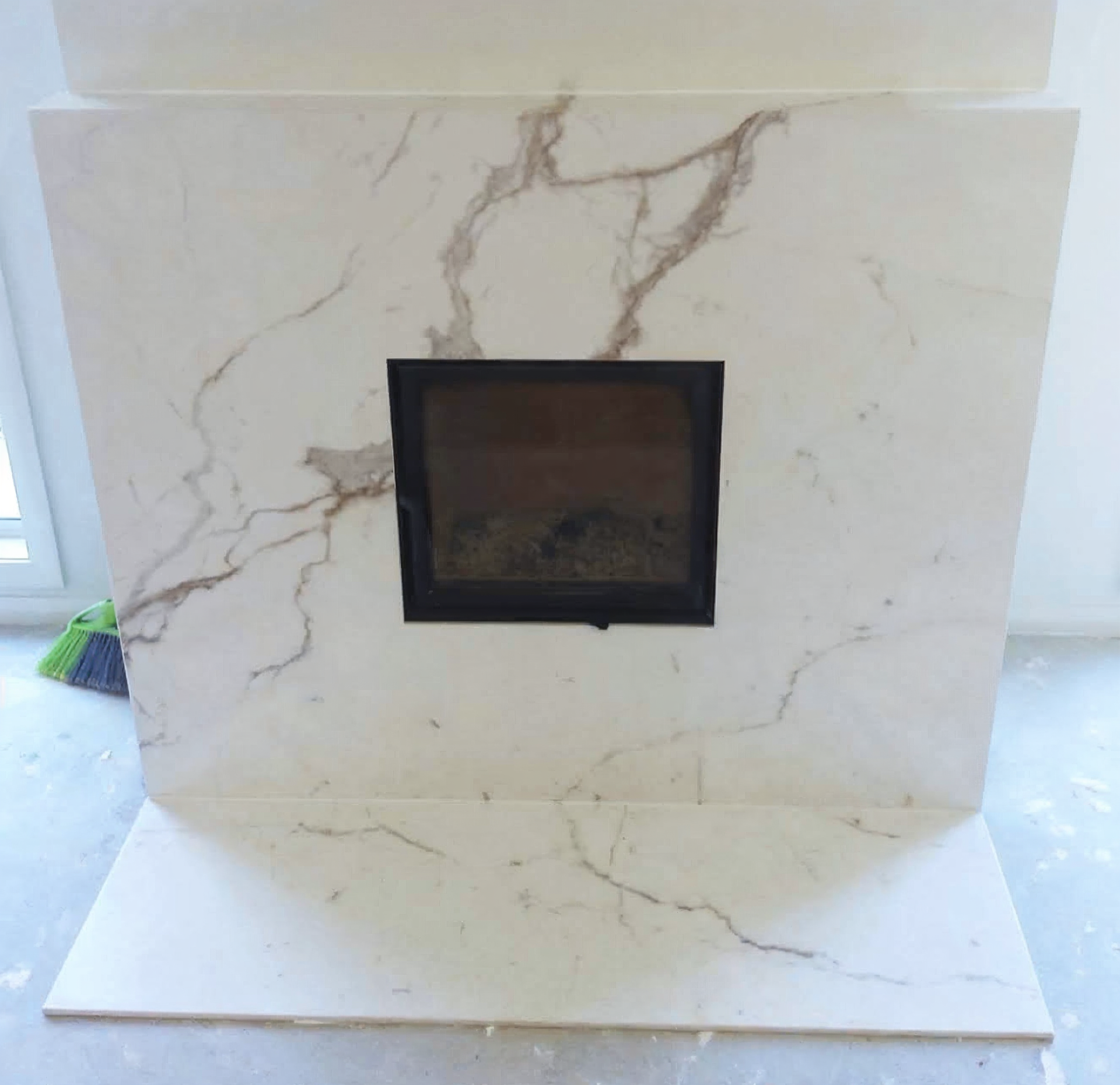 White marble fireplace with a black-framed square firebox opening.