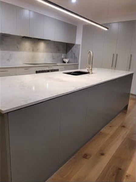 Modern kitchen with gray cabinets, white island countertop, built-in sink, and wood flooring