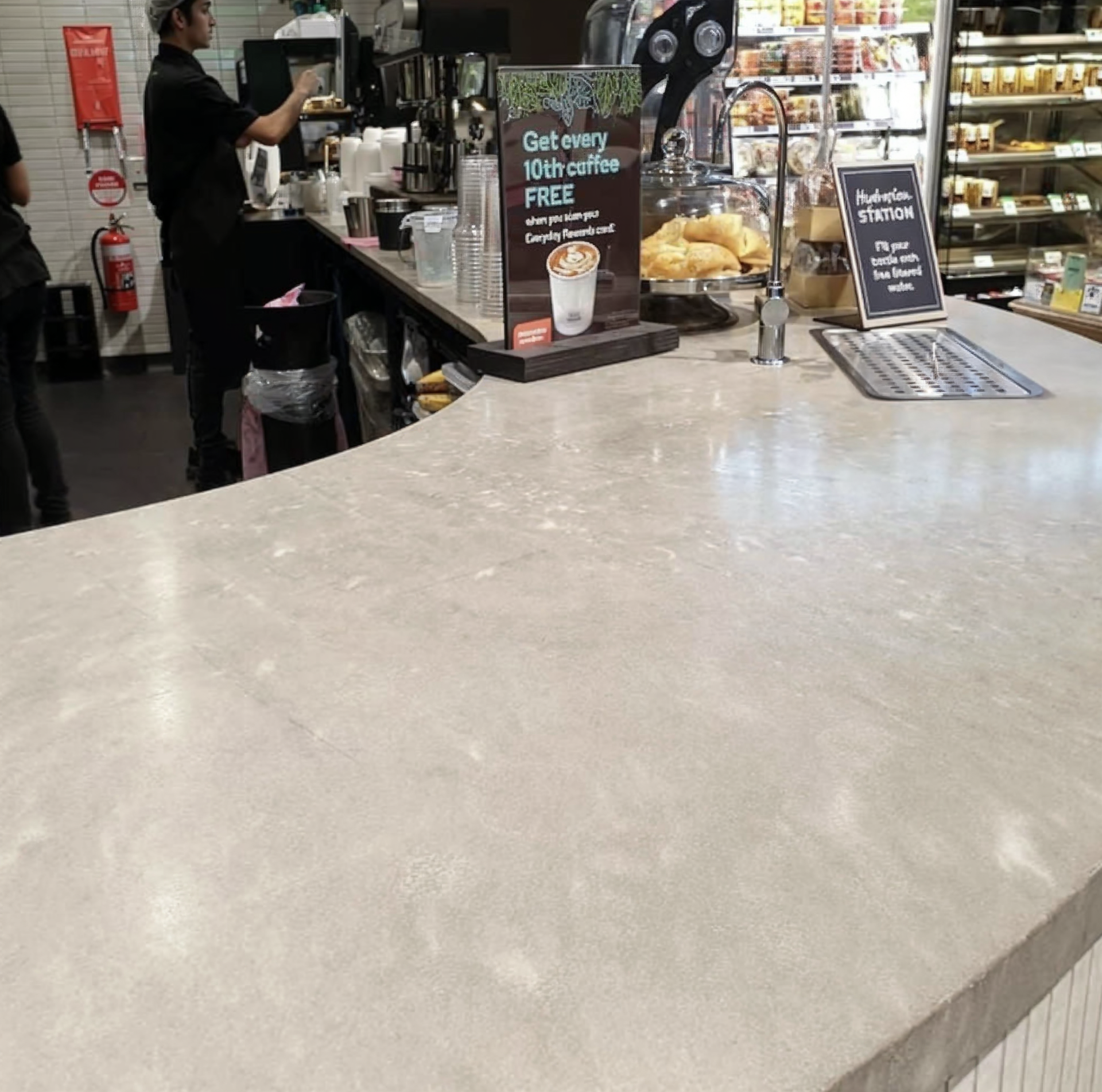 Grocery store café counter with a cashier, pastry display, and large empty countertop in the foreground