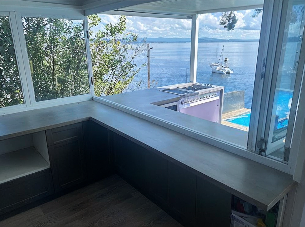 Covered porch overlooking a calm ocean with a small boat and blue pool below