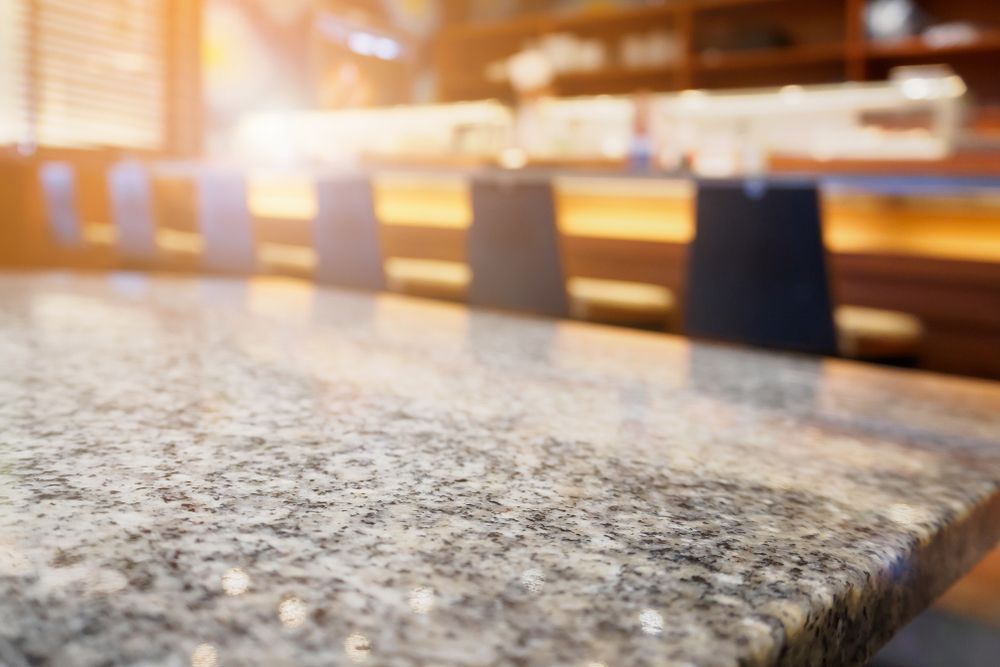 Polished granite countertop in a softly lit restaurant or bar with blurred chairs in the background