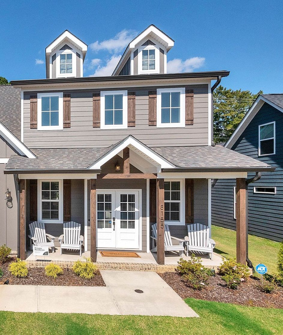 Two-story home with gray James Hardie siding, wood shutters, white trim, dormer windows, and a front porch with Adirondack chairs