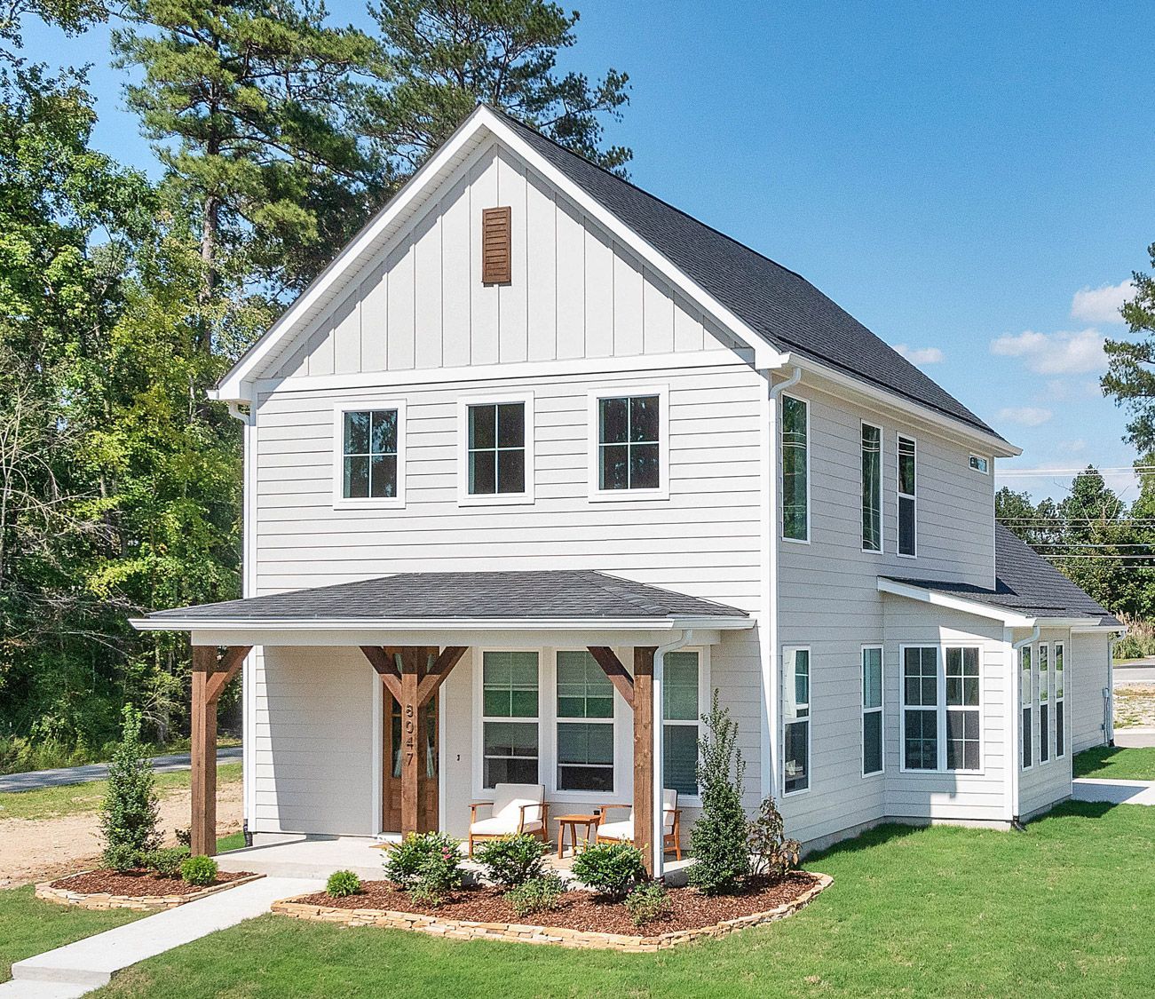 Two-story modern farmhouse with white James Hardie siding, black roof, wood porch posts, and landscaped front yard
