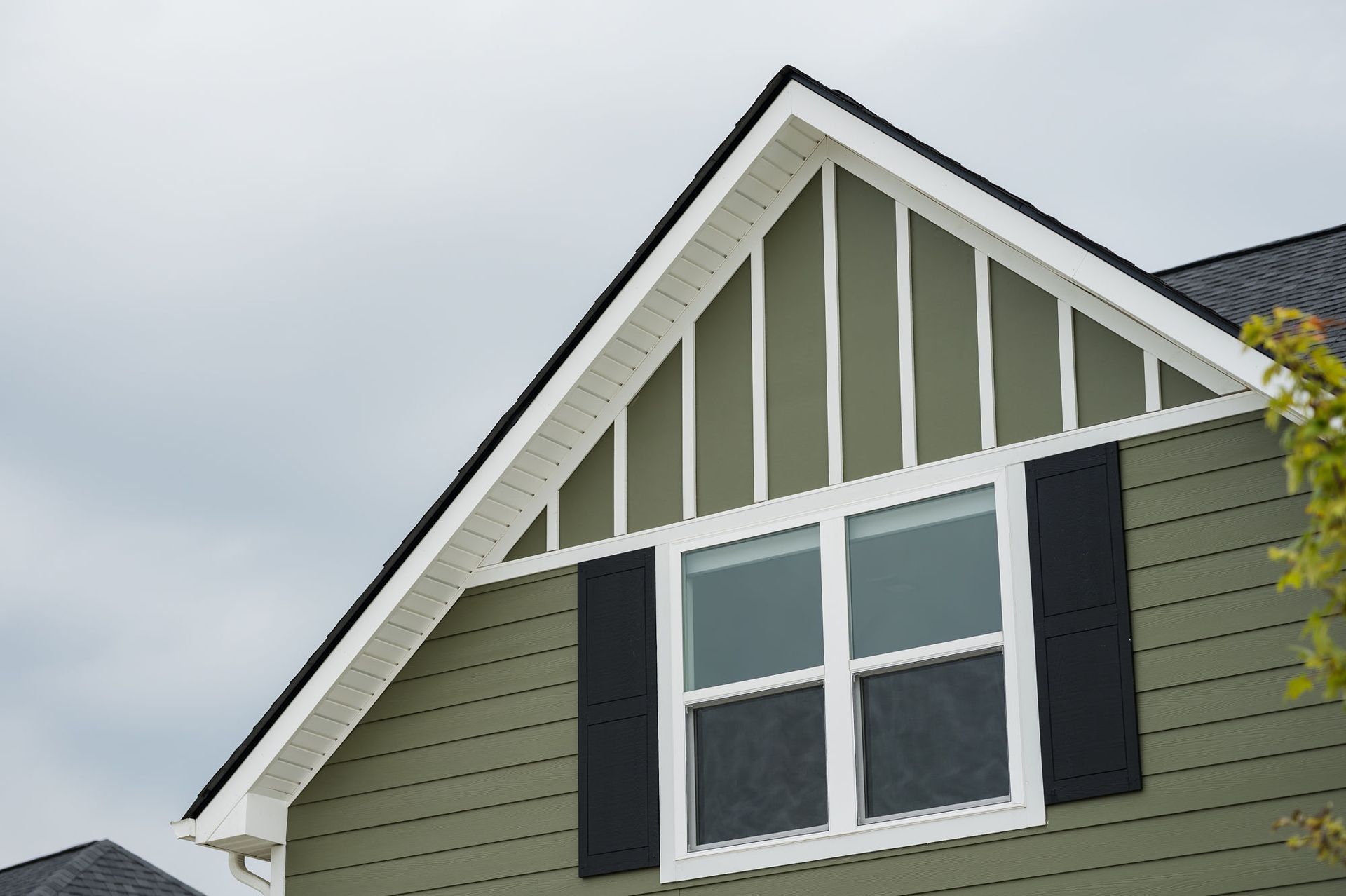 Close-up of a house with green siding, white trim, black shutters, and a gable roof, showing exterior siding detail for porch enclosures in Chattanooga