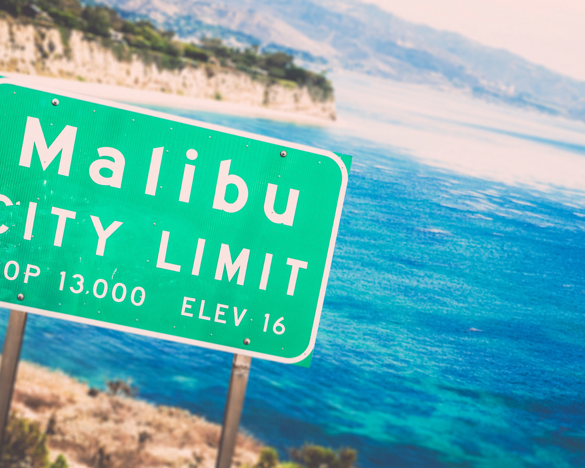 Green Malibu City Limit sign overlooking the ocean and cliffs.