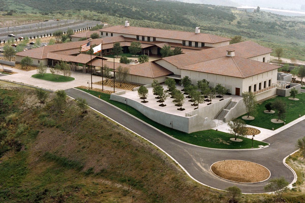 Aerial view of a beige building complex with a brown roof and a circular driveway on a hillside.