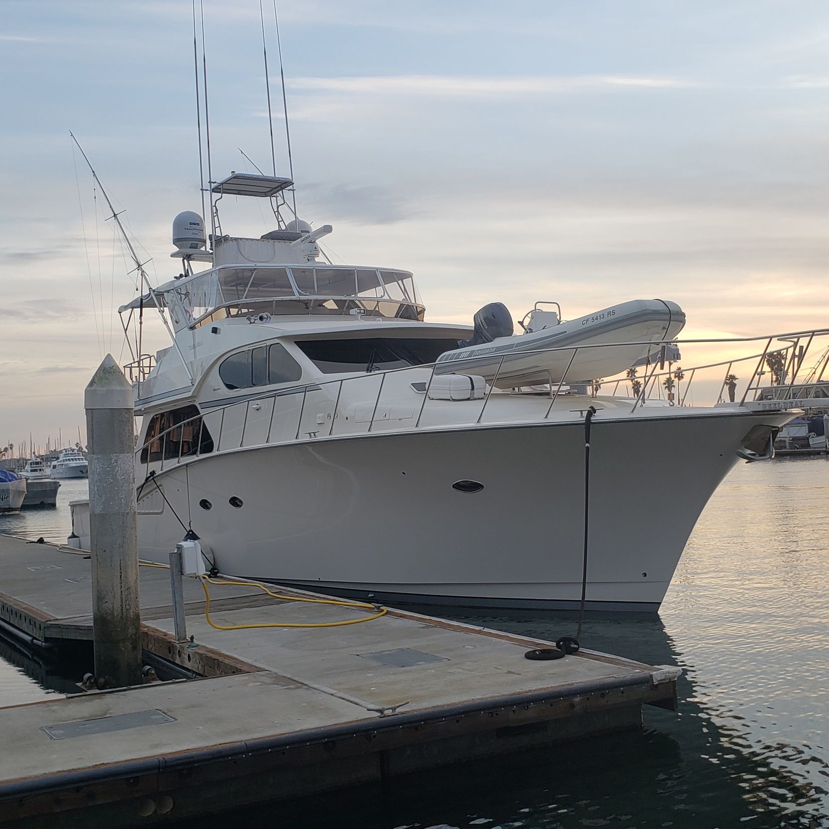 White yacht docked at a harbor, masts and radar visible. Sunset in the background.