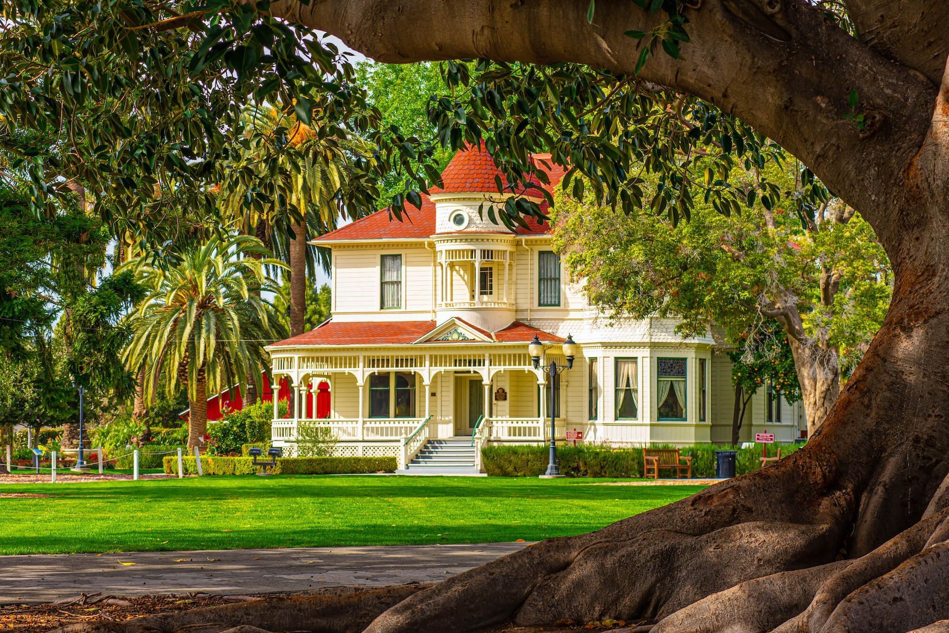 Victorian house with red roof, porch, and green lawn framed by a large tree.